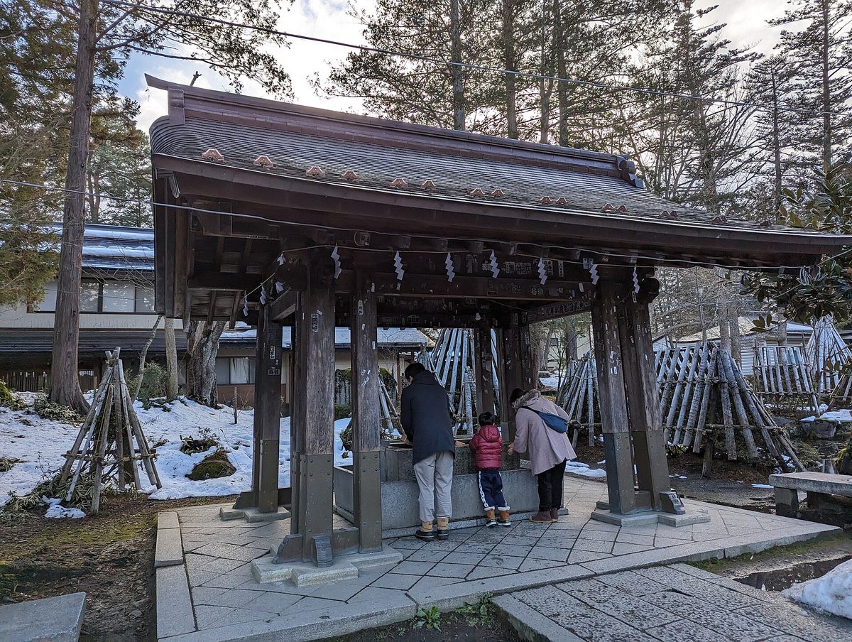 雪の残る上杉神社境内の手水舎で手水をとる参拝者