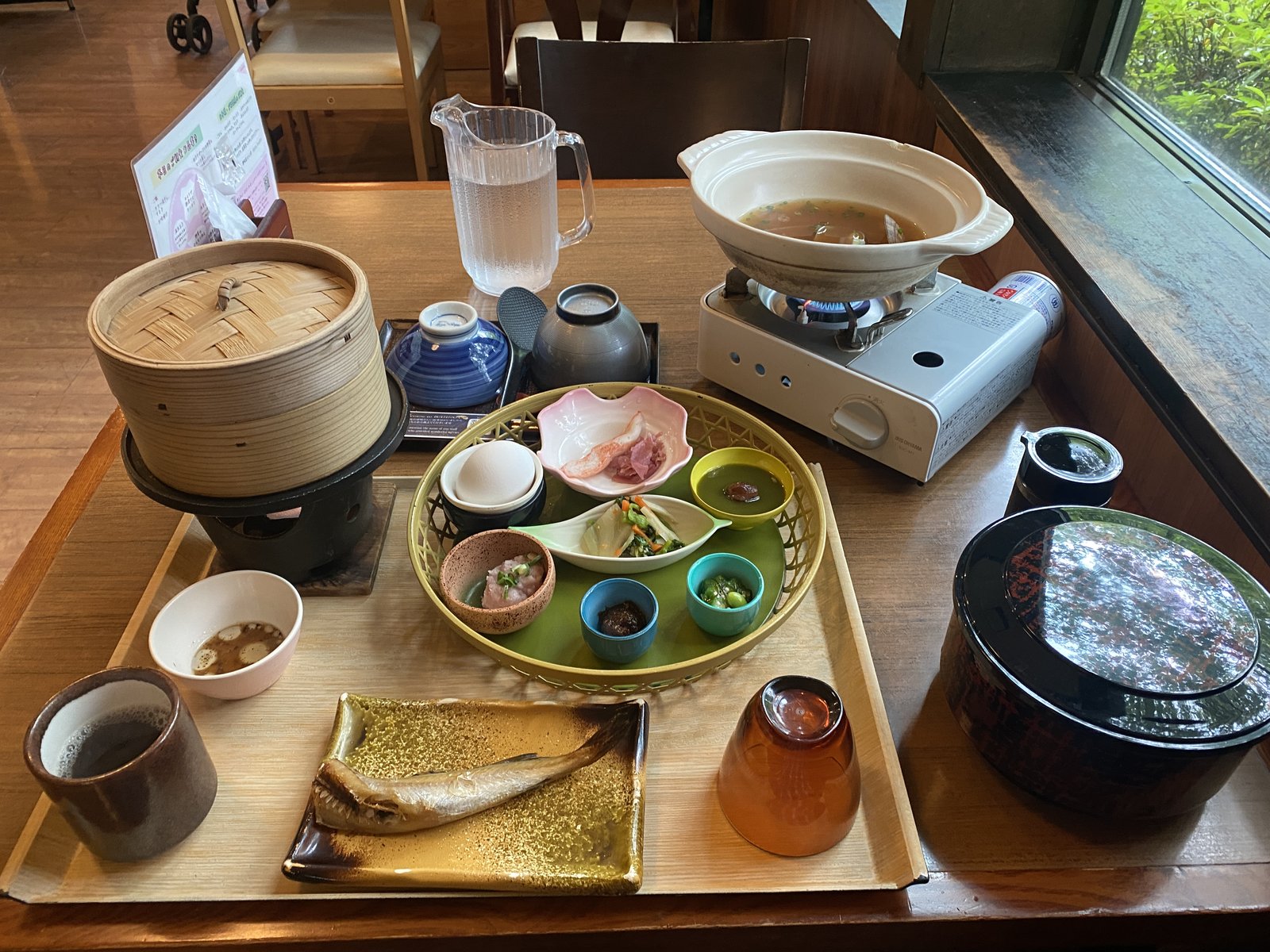 品の木一の湯の朝食全景（タラの一夜干し・かご盛り小鉢・せいろ蒸し・土鍋の味噌汁・おひつご飯）